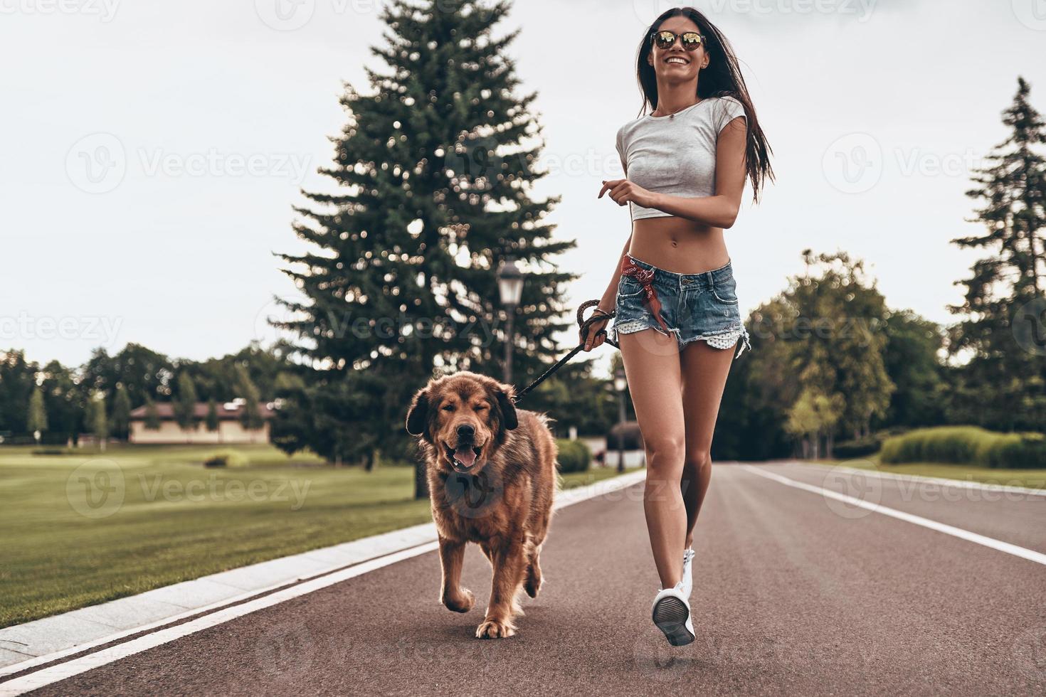 Full length of beautiful young woman running with her dog through the park and smiling while spending time outdoors photo