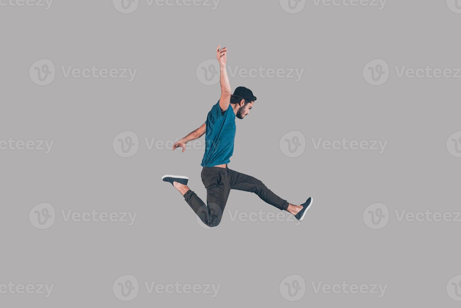 Like a rock star. Mid-air shot of handsome young man in cap jumping and gesturing against background photo