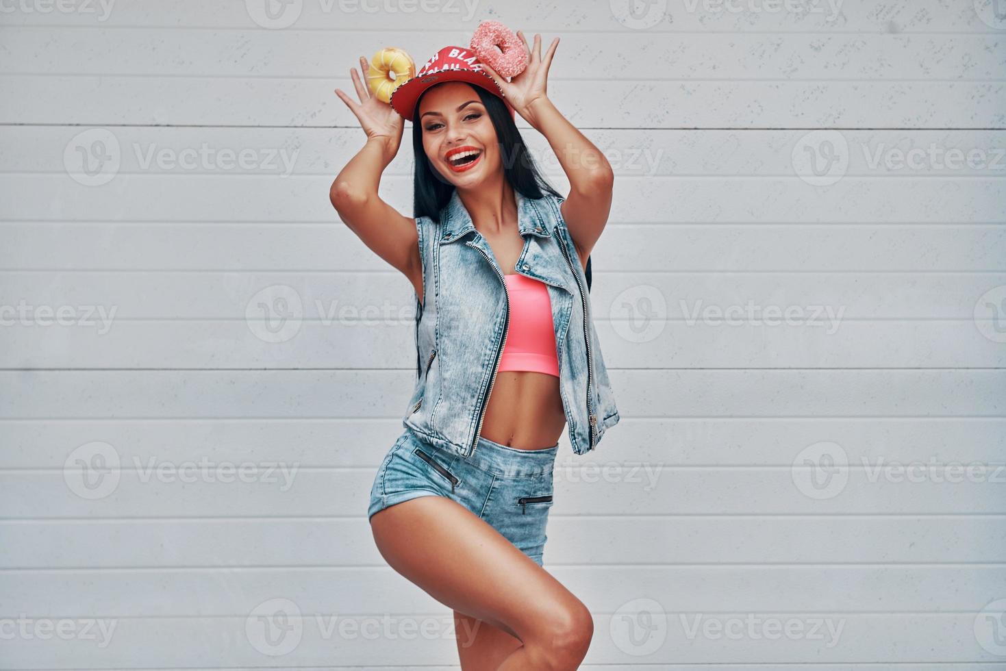 Adding some fun to her day. Cheerful young women holding donuts above her head and smiling while standing against the garage door photo