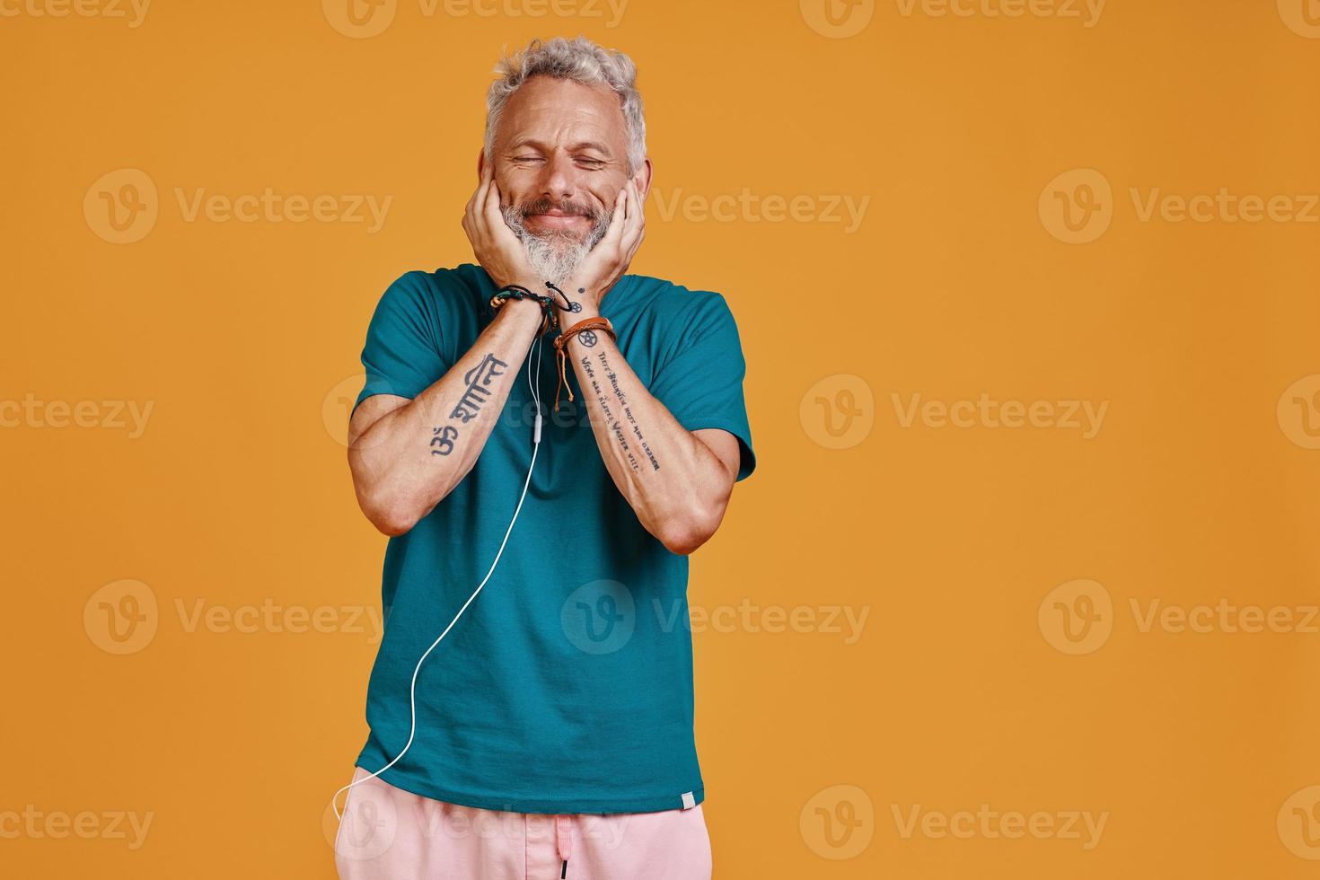 Happy senior man listening music and smiling while standing against orange background photo
