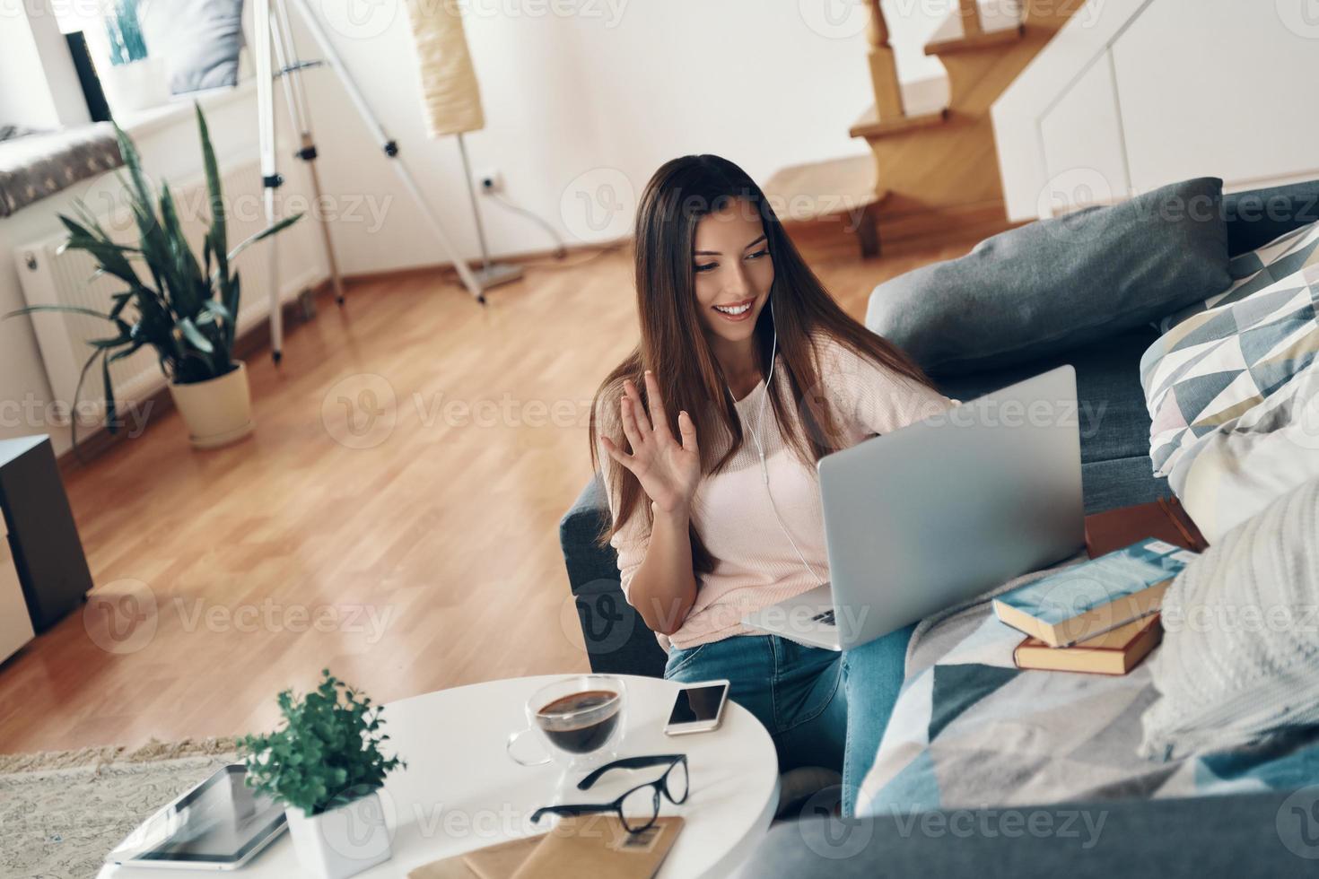 Beautiful young woman in casual clothing talking to someone using laptop while resting at home photo
