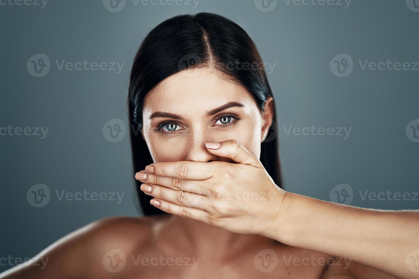 Beautiful young woman looking at camera and covering mouth with hand photo