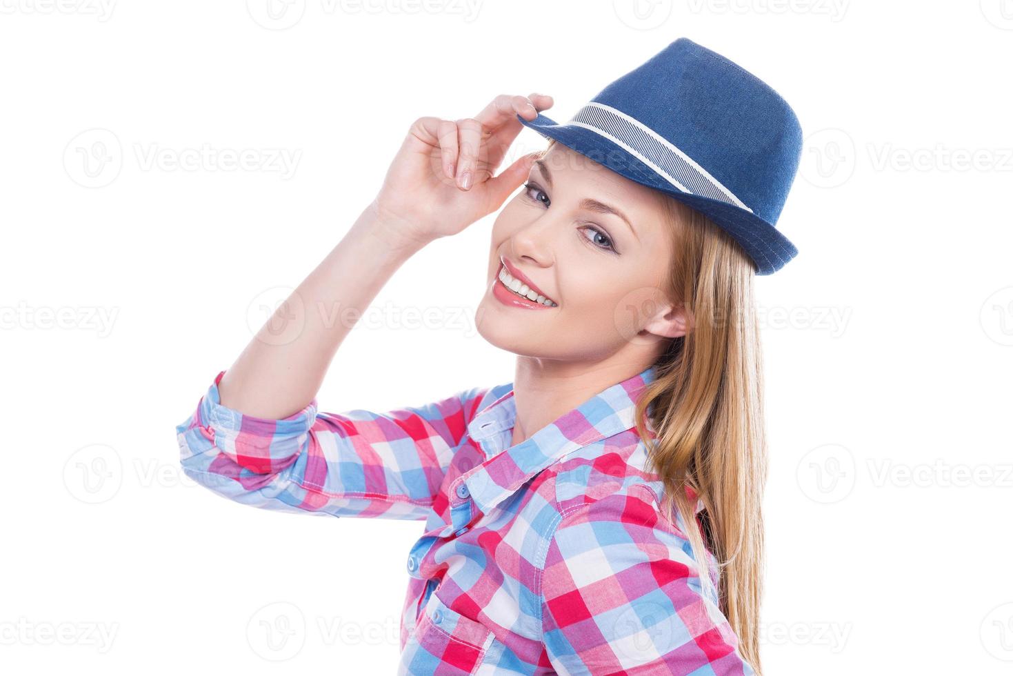 Funky style. Beautiful young woman in funky wear adjusting her hat and looking at camera while standing against white background photo