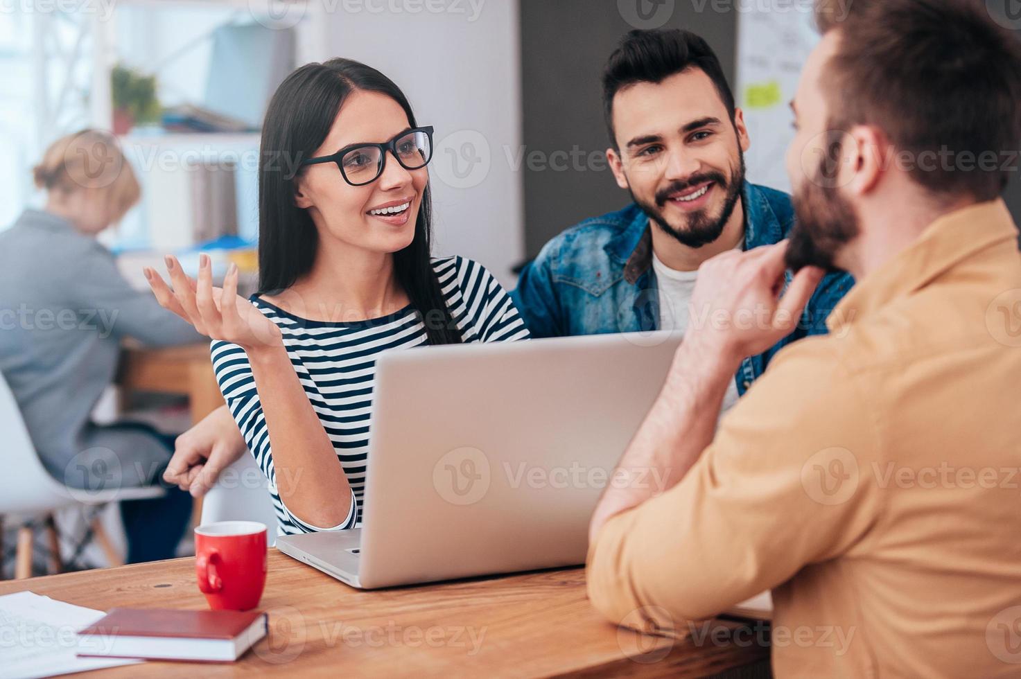 Discussing new project together. Cheerful young people discussing something while sitting at the desk in office photo