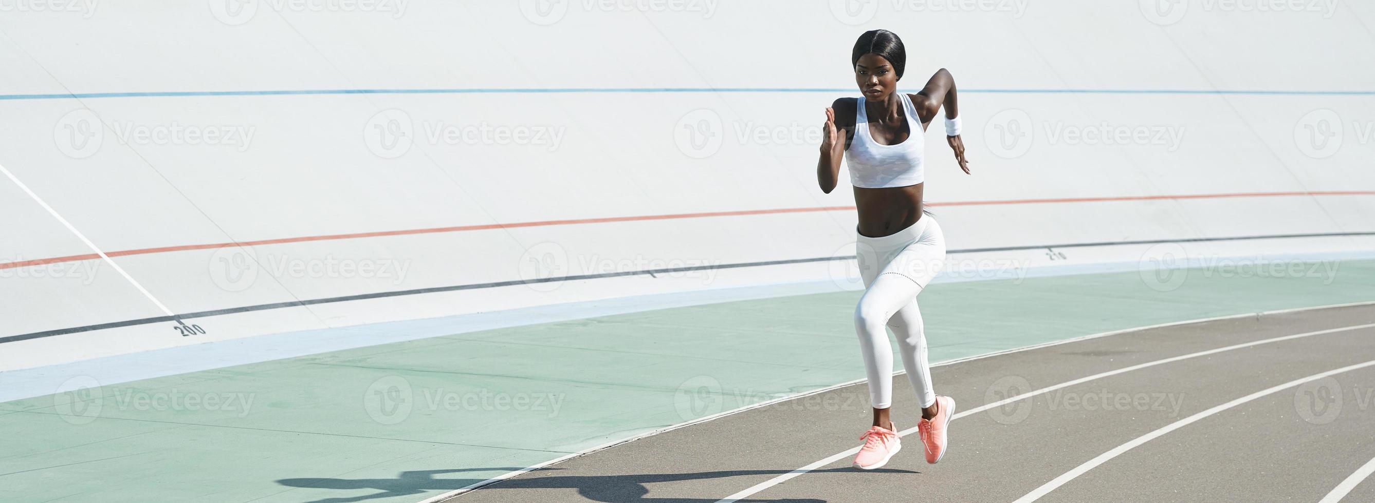 Beautiful young African woman in sports clothing running on track outdoors photo