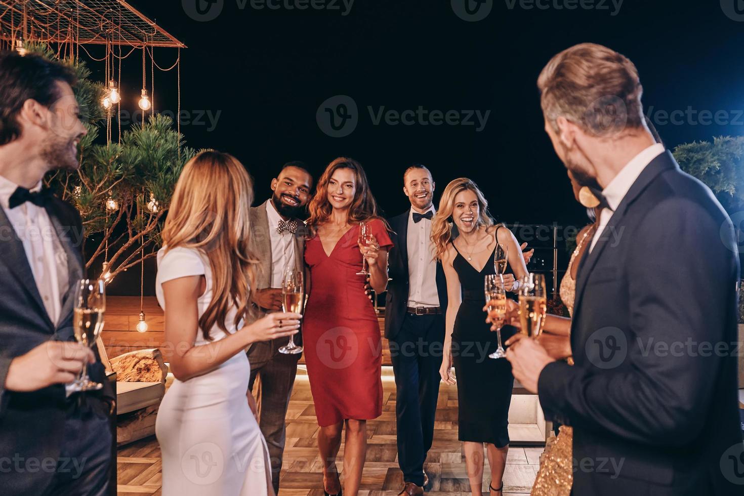 grupo de personas hermosas en ropa formal comunicándose y sonriendo mientras pasan tiempo en una fiesta de lujo foto