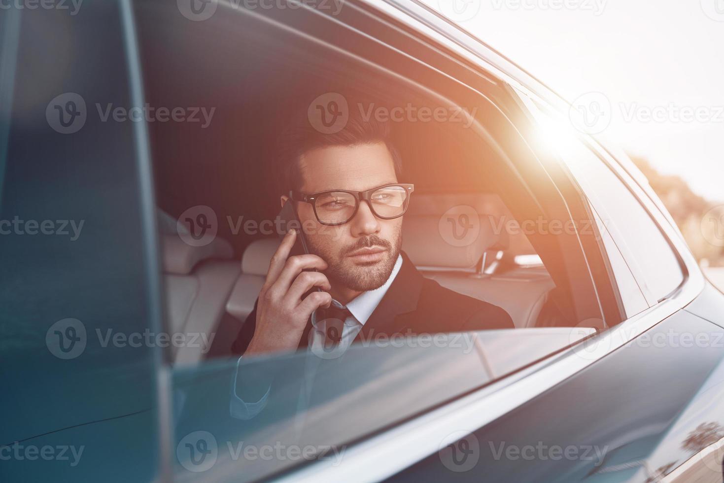 Discussing business details. Thoughtful young businessman talking on the phone while sitting in the car photo