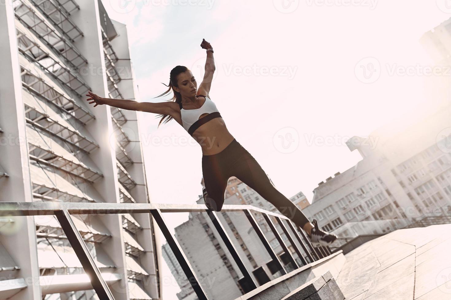 Everything is possible. Full length of modern young woman in sports clothing jumping while exercising outdoors photo