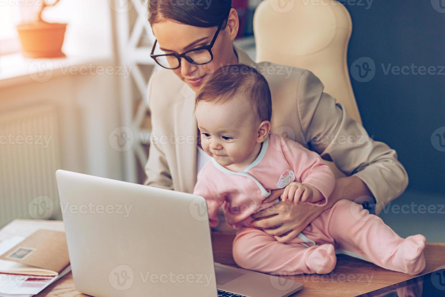 pequeño asistente. niñita usando una laptop mientras se sienta en el escritorio de la oficina con su madre en la oficina foto