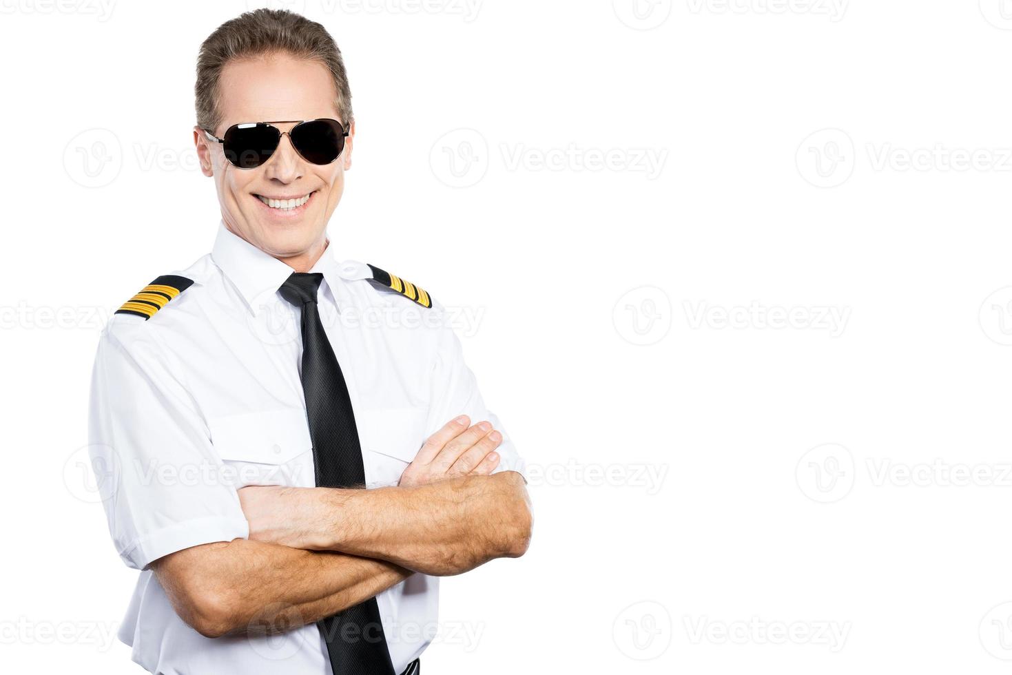 Confident pilot. Confident male pilot in uniform keeping arms crossed and smiling while standing against white background photo