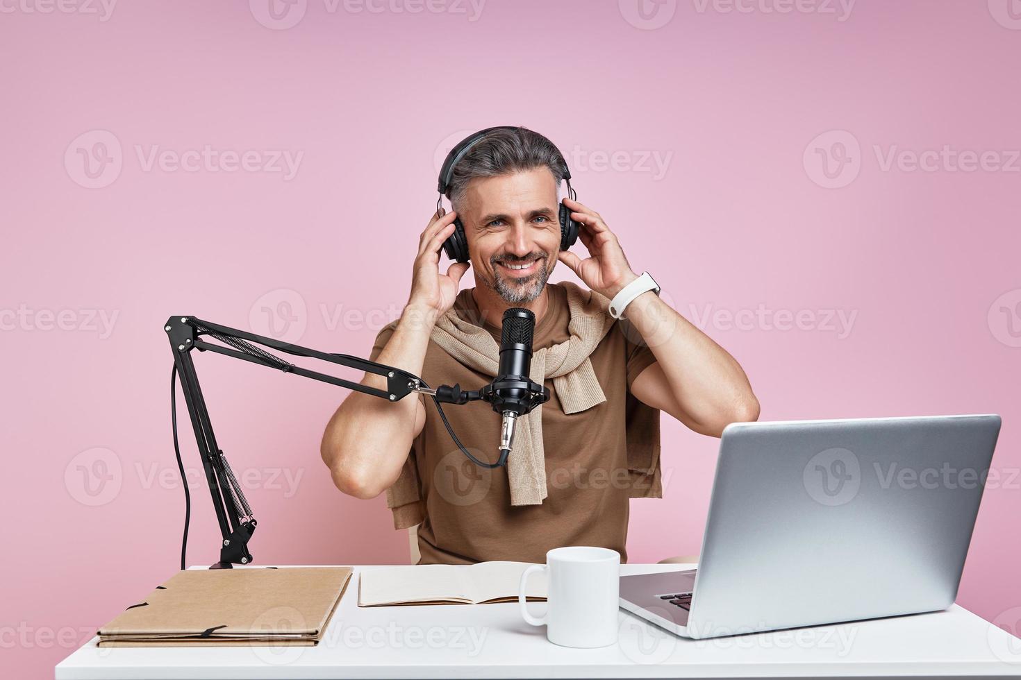 Cheerful man in headphones using microphone while recording podcast against pink background photo