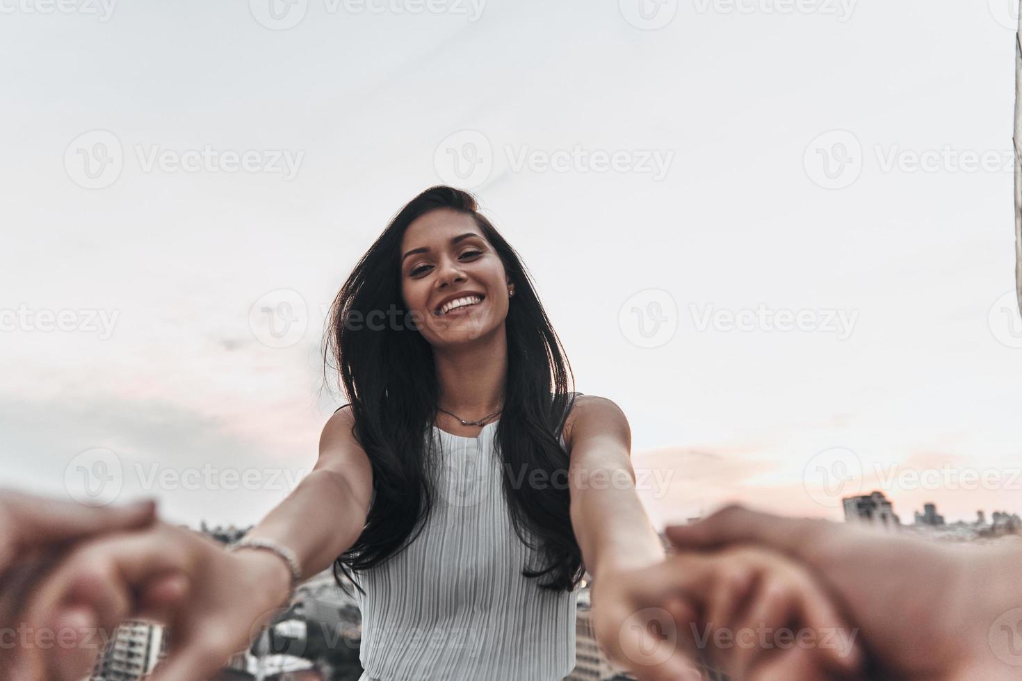 Happy to be in love. Beautiful young woman smiling and looking at camera while holding hands with her boyfriend outdoors photo