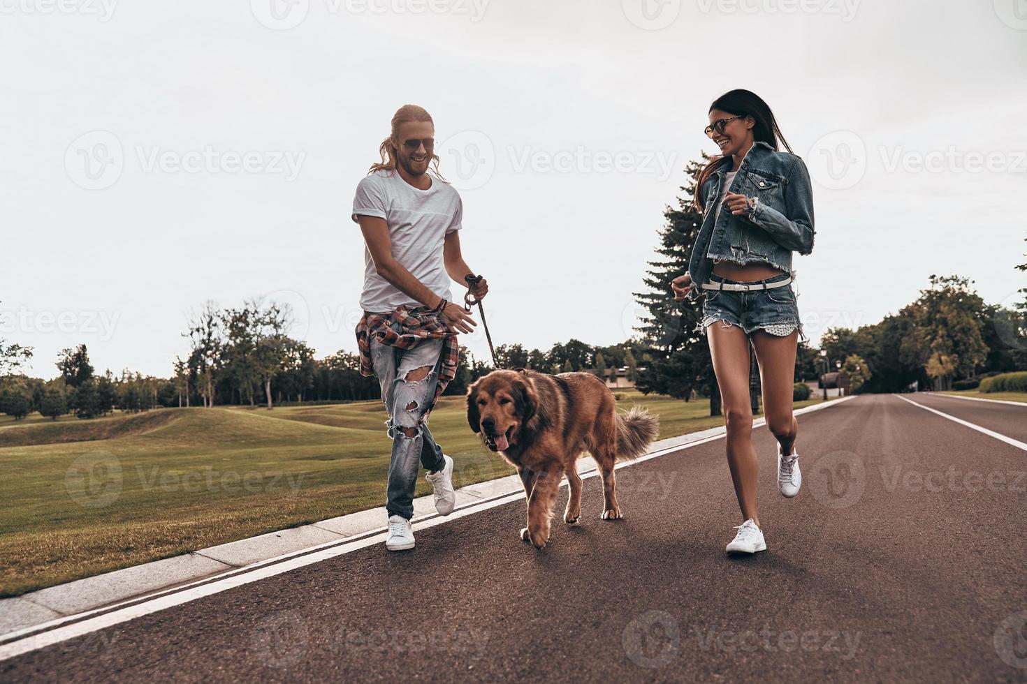 Full length of beautiful young couple running with their dog while spending time outdoors photo