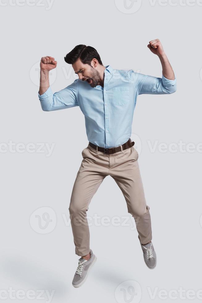 Always winning.  Full length of handsome young man gesturing and shouting while jumping grey background photo