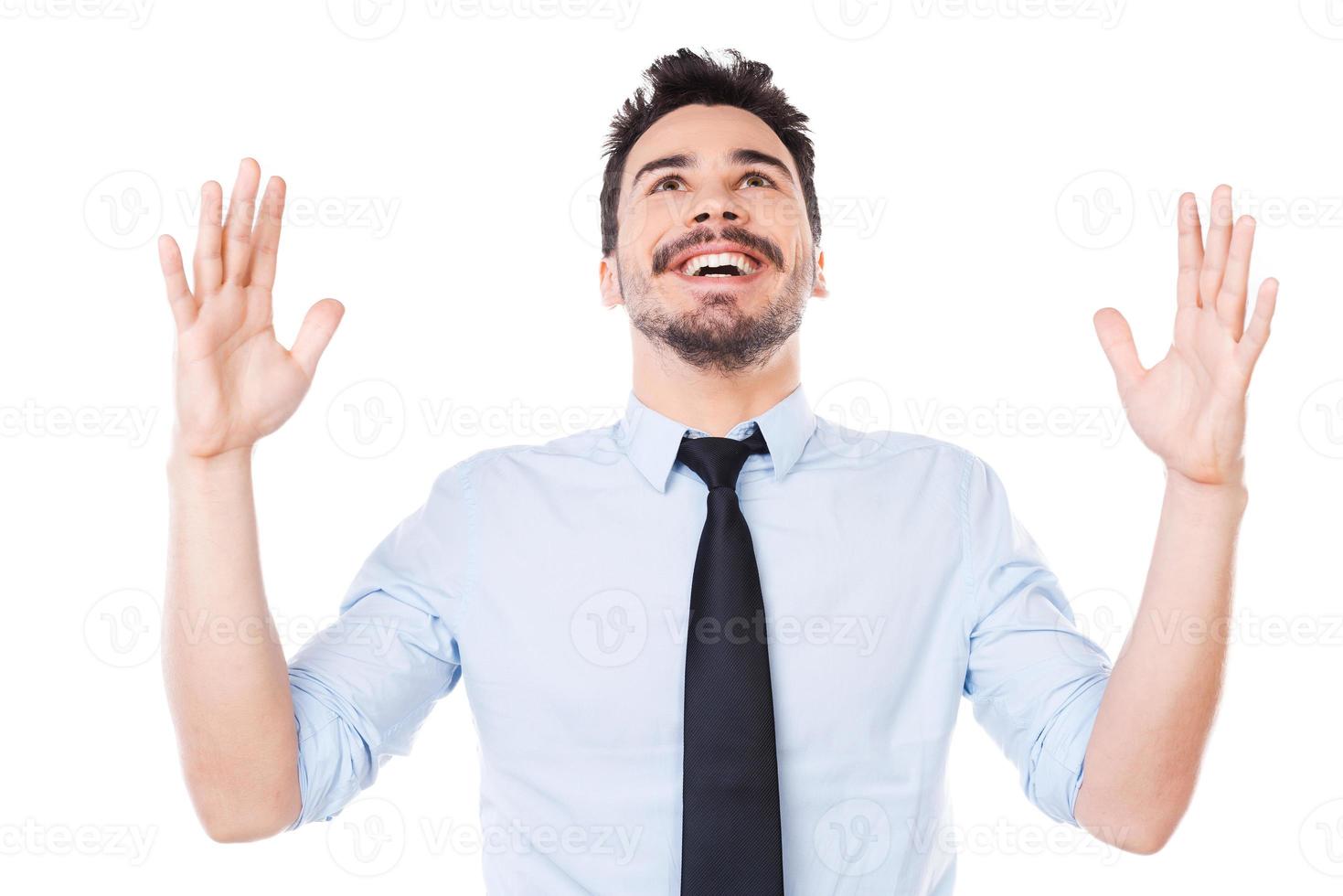 Hombre de negocios exitoso. joven feliz con camisa y corbata manteniendo los brazos levantados y sonriendo mientras está de pie contra el fondo blanco foto