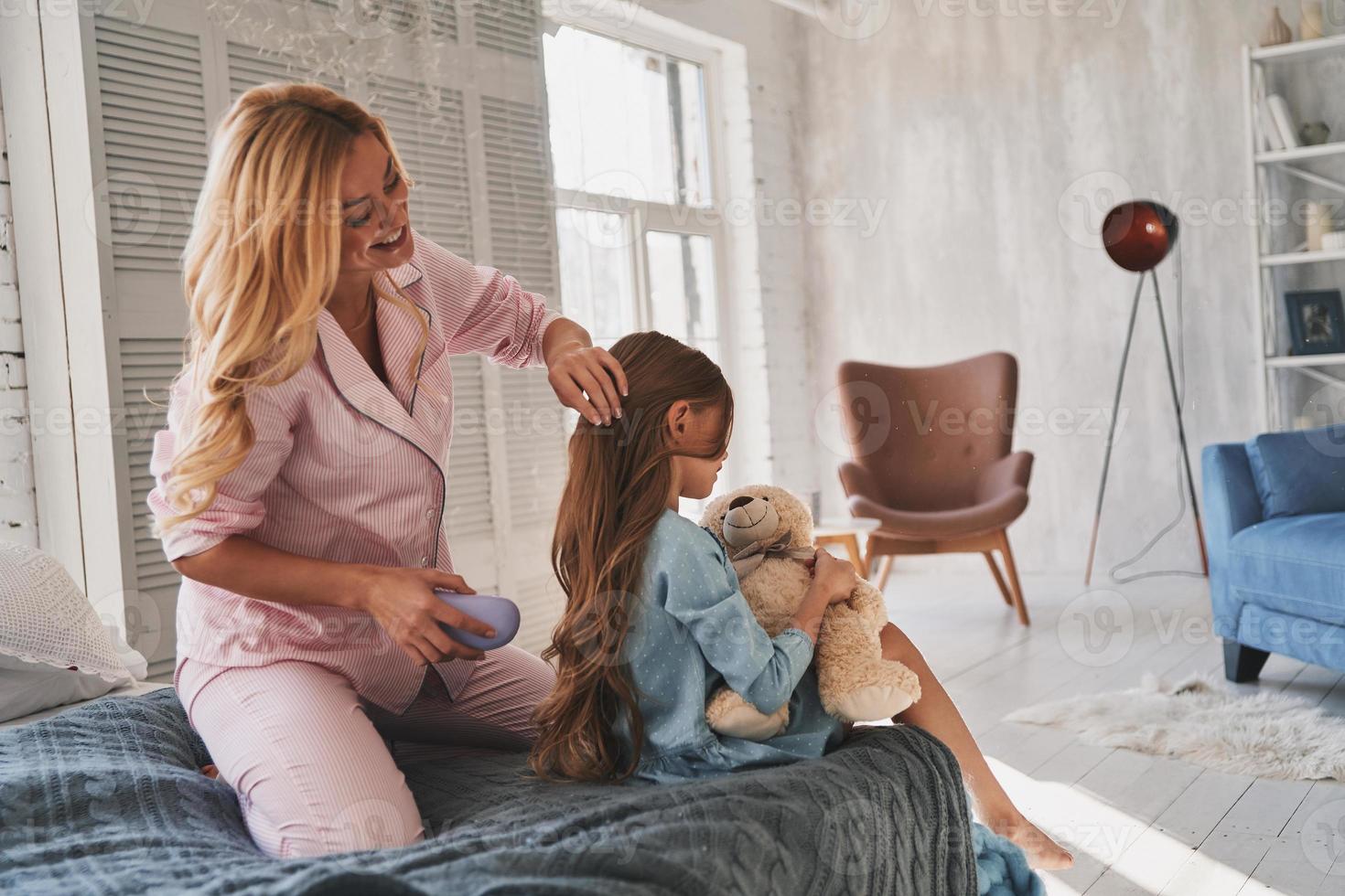 Mother Care Beautiful Young Mother Brushing Her Daughters Hair While Sitting On The Bed At Home 