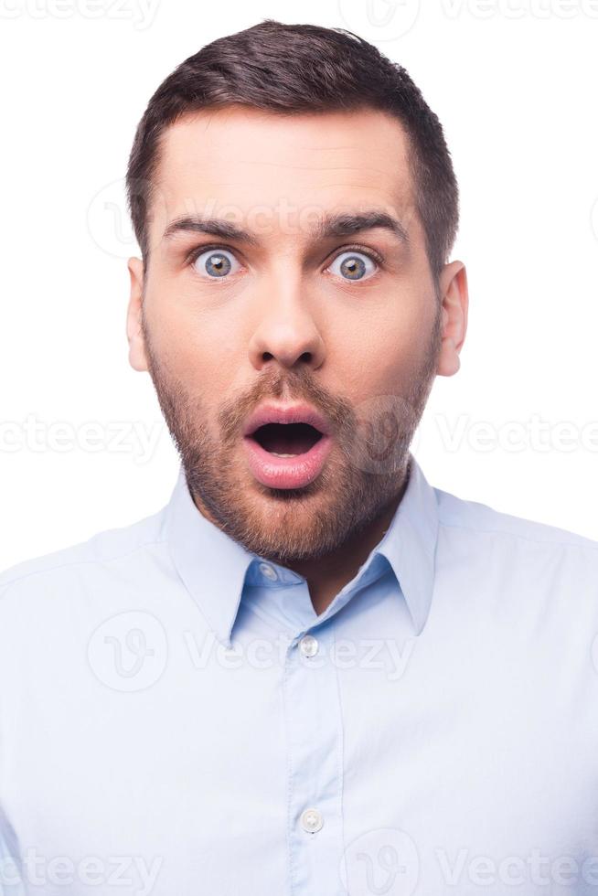 Shocking news. Portrait of surprised young man in shirt staring at camera while standing against white background photo