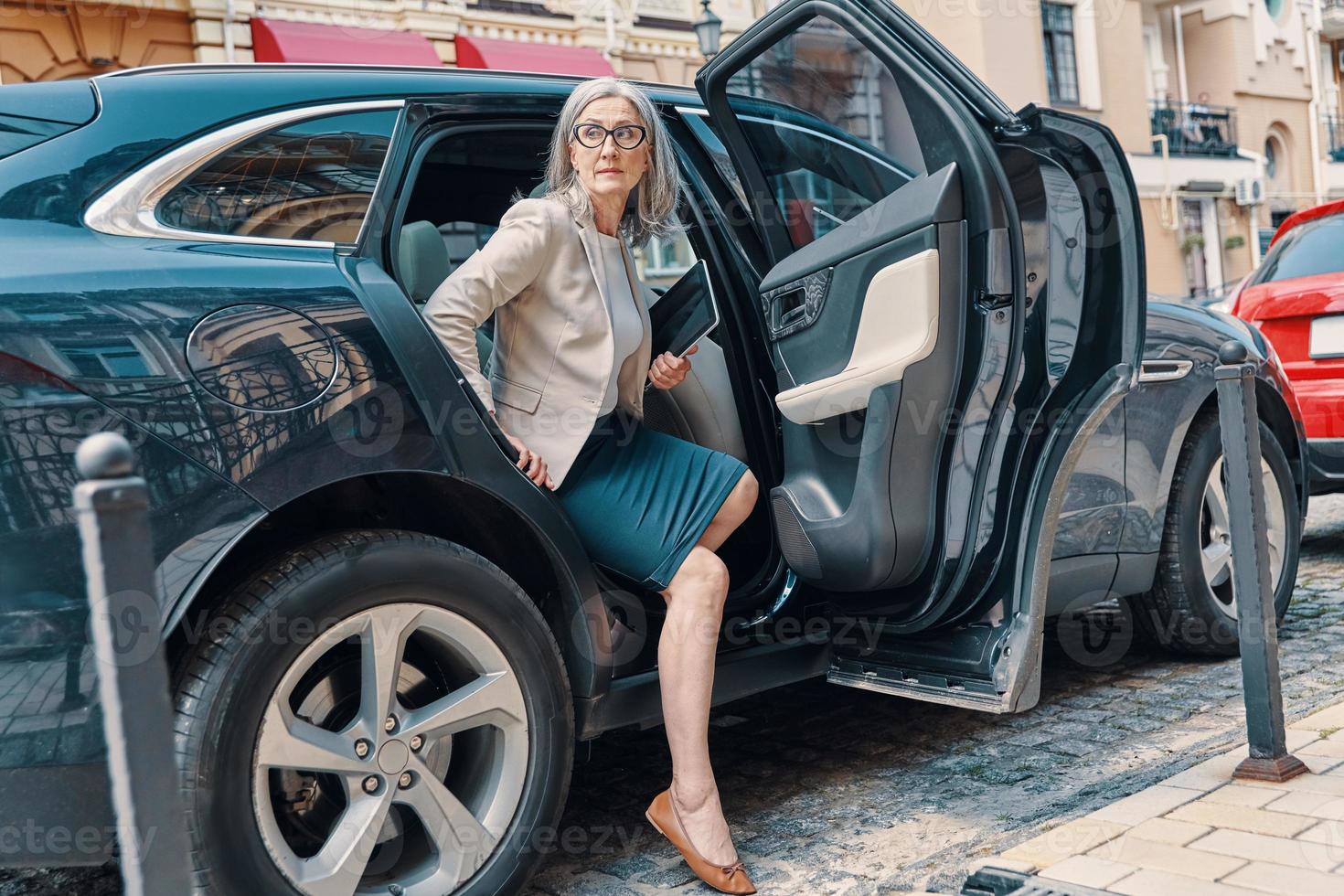 hermosa mujer madura con ropa informal elegante mirando hacia otro lado mientras sale del auto al aire libre foto