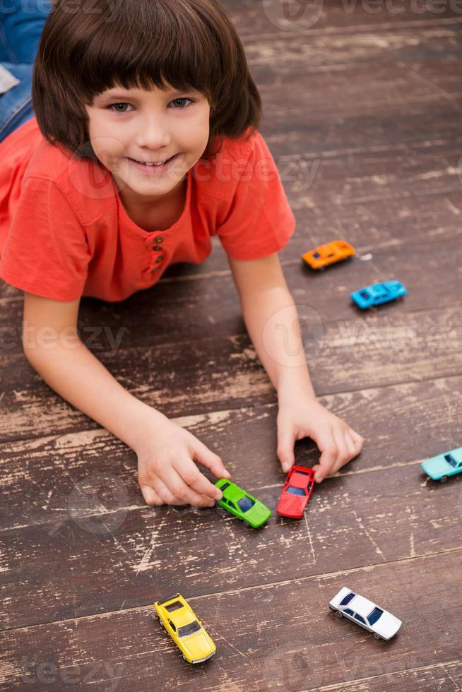 The best spending of free time. Picture of little boy lying on the floor and playing with toy cars photo