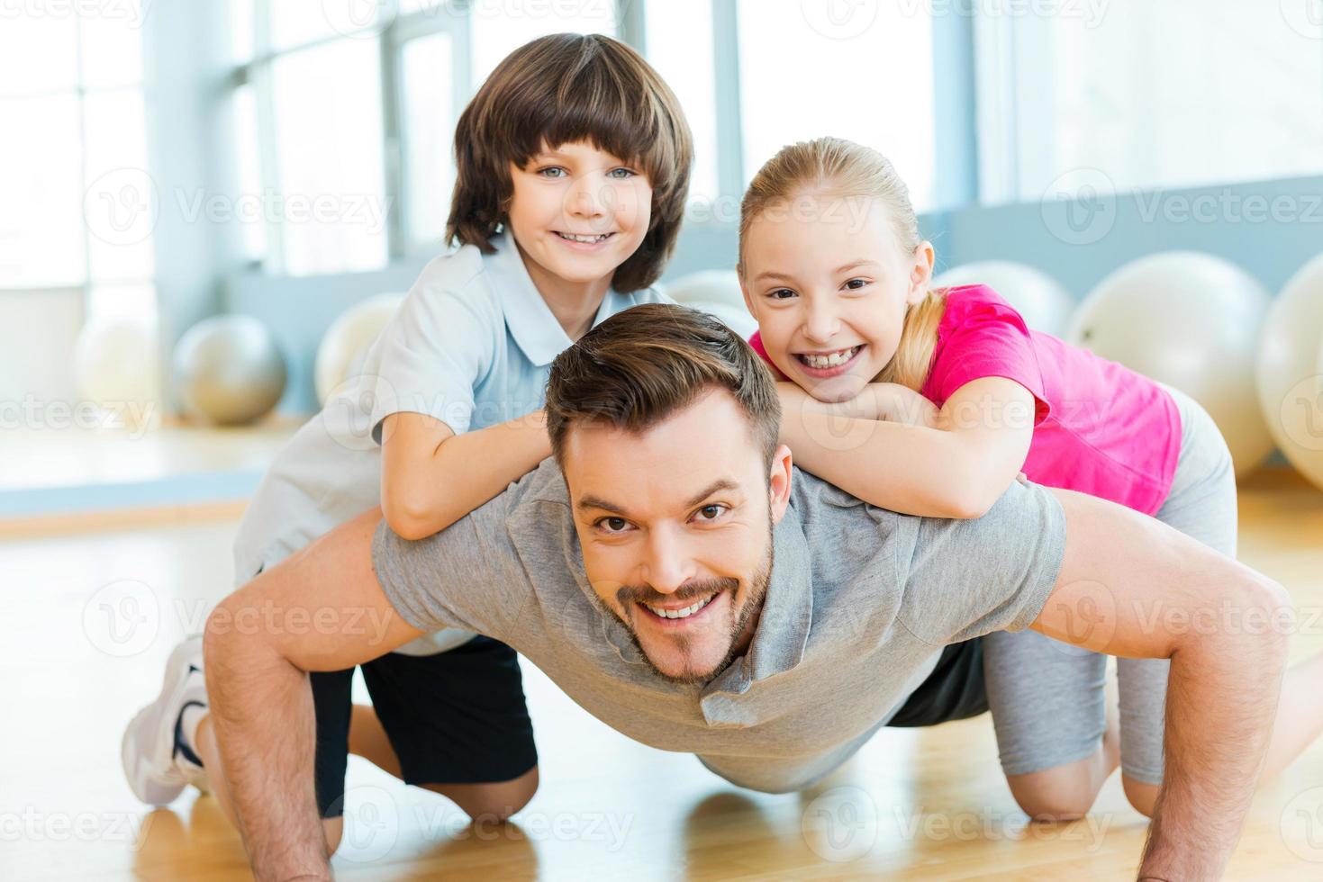 haciendo ejercicio con el padre. niños pequeños felices uniéndose a su padre haciendo flexiones en el club deportivo foto