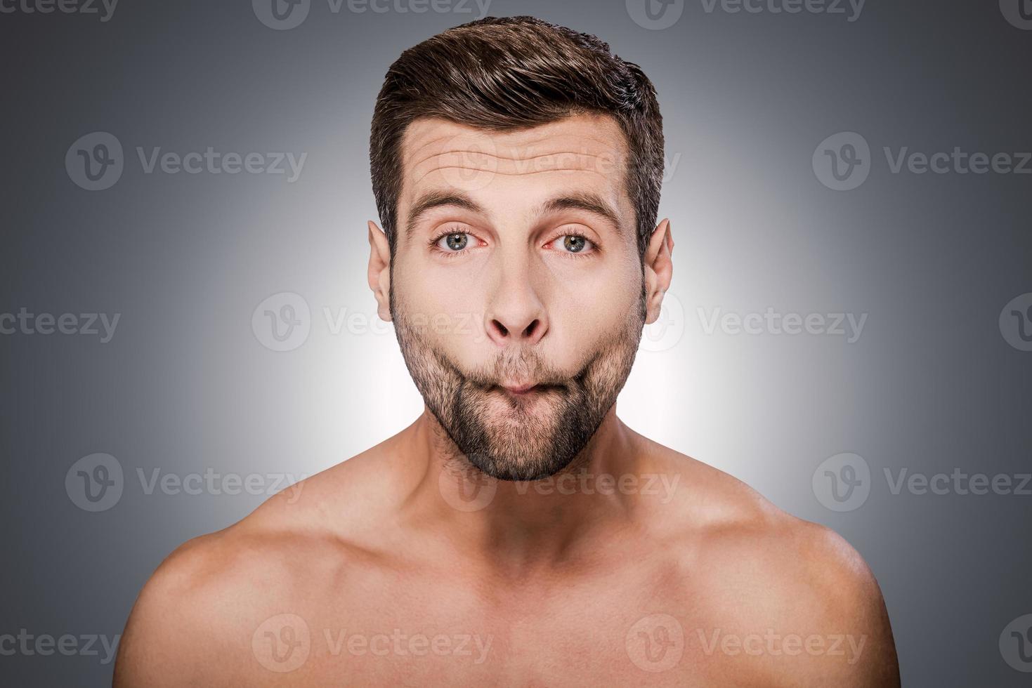 Feeling playful. Portrait of handsome young shirtless man looking at camera and grimacing while standing against grey background photo