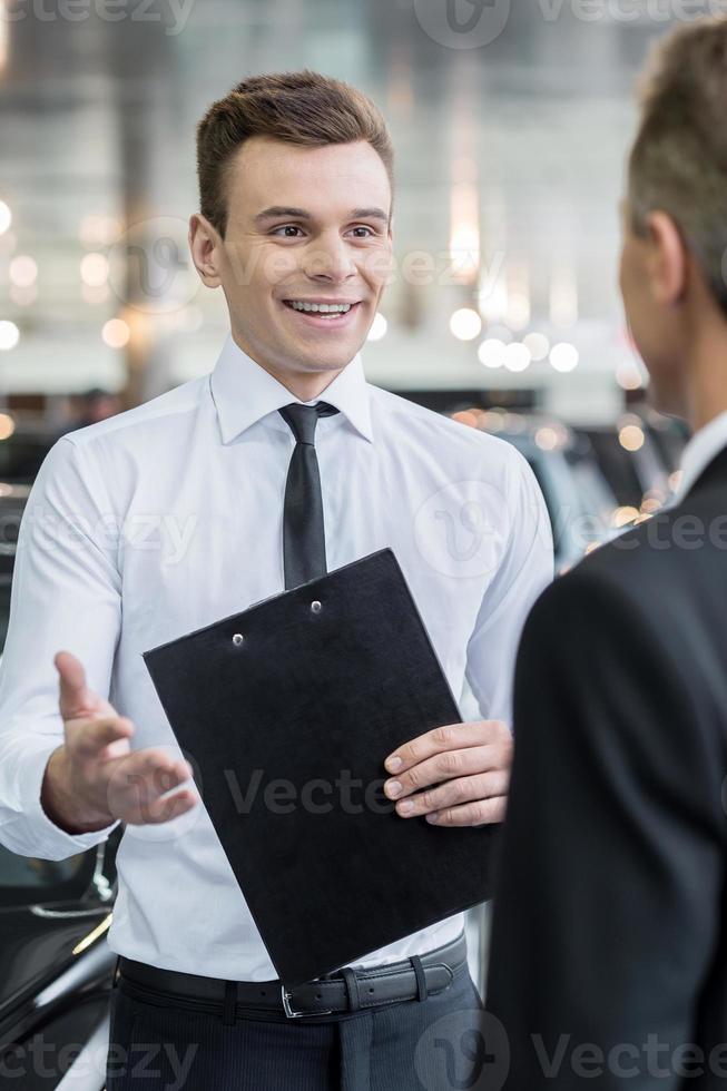 Salesman and customer. Handsome young classic car salesman talking to a customer and smiling