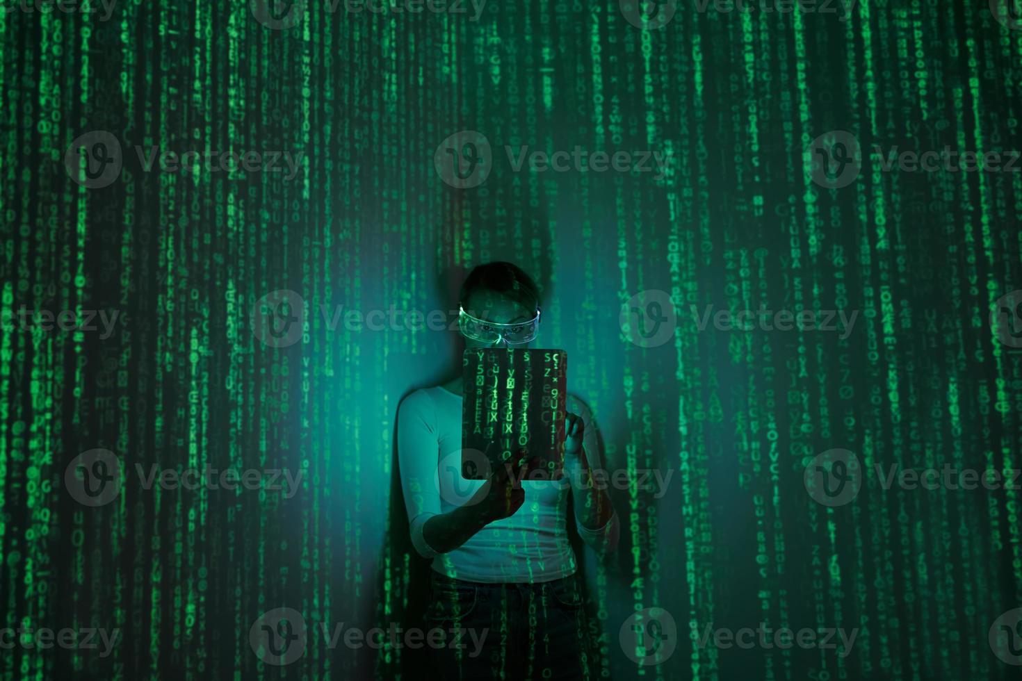 Woman in futuristic glasses using digital tablet against dark background with green symbols photo