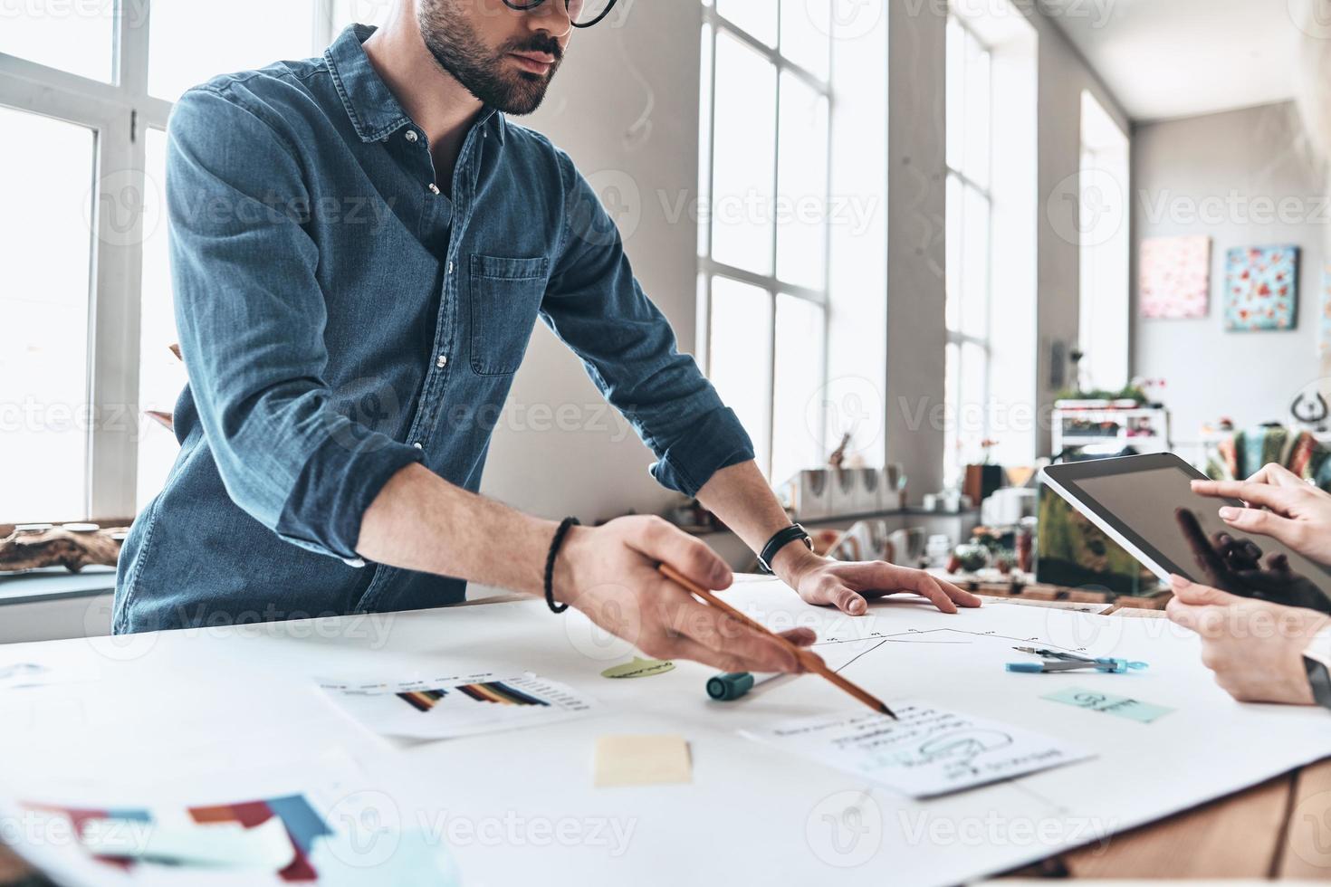 Discussing business. Close up of young modern people in smart casual wear using blueprint while working in the creative working space photo