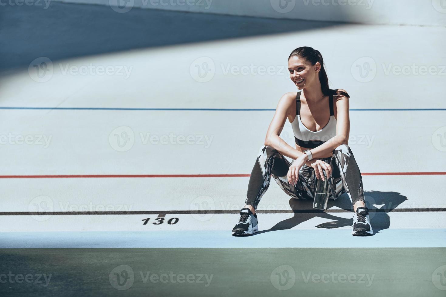 Never give up. Beautiful young woman in sports clothing looking away while sitting on the running track outdoors photo