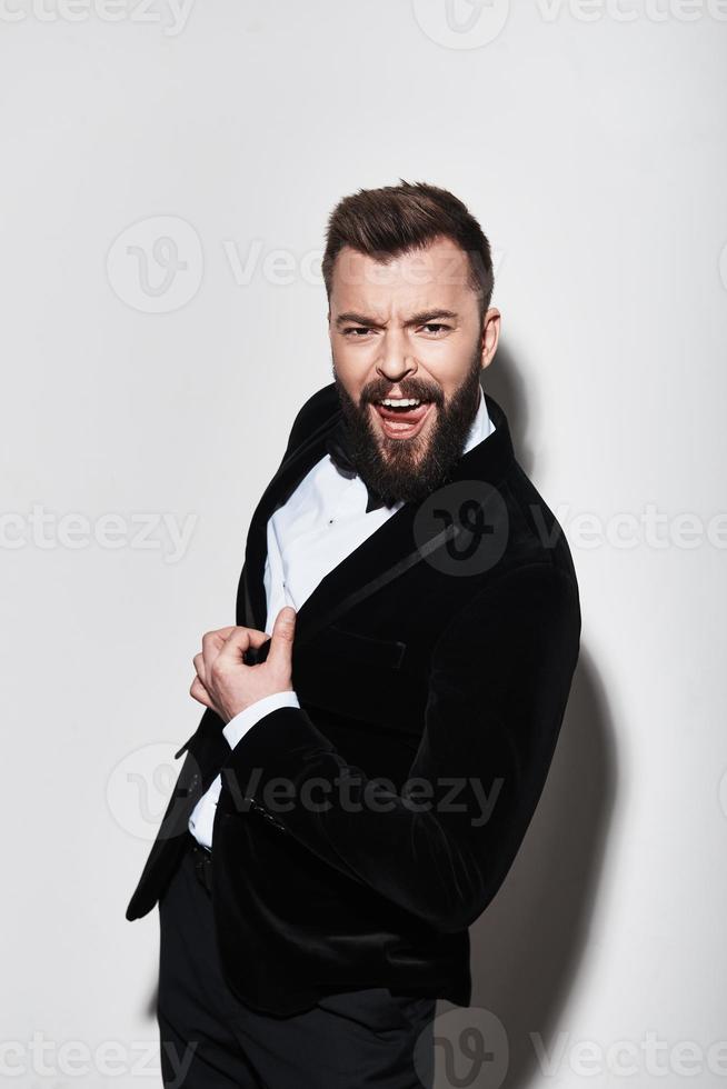 Pure confidence. Handsome young man in full suit making a face and looking at camera while standing against grey background photo