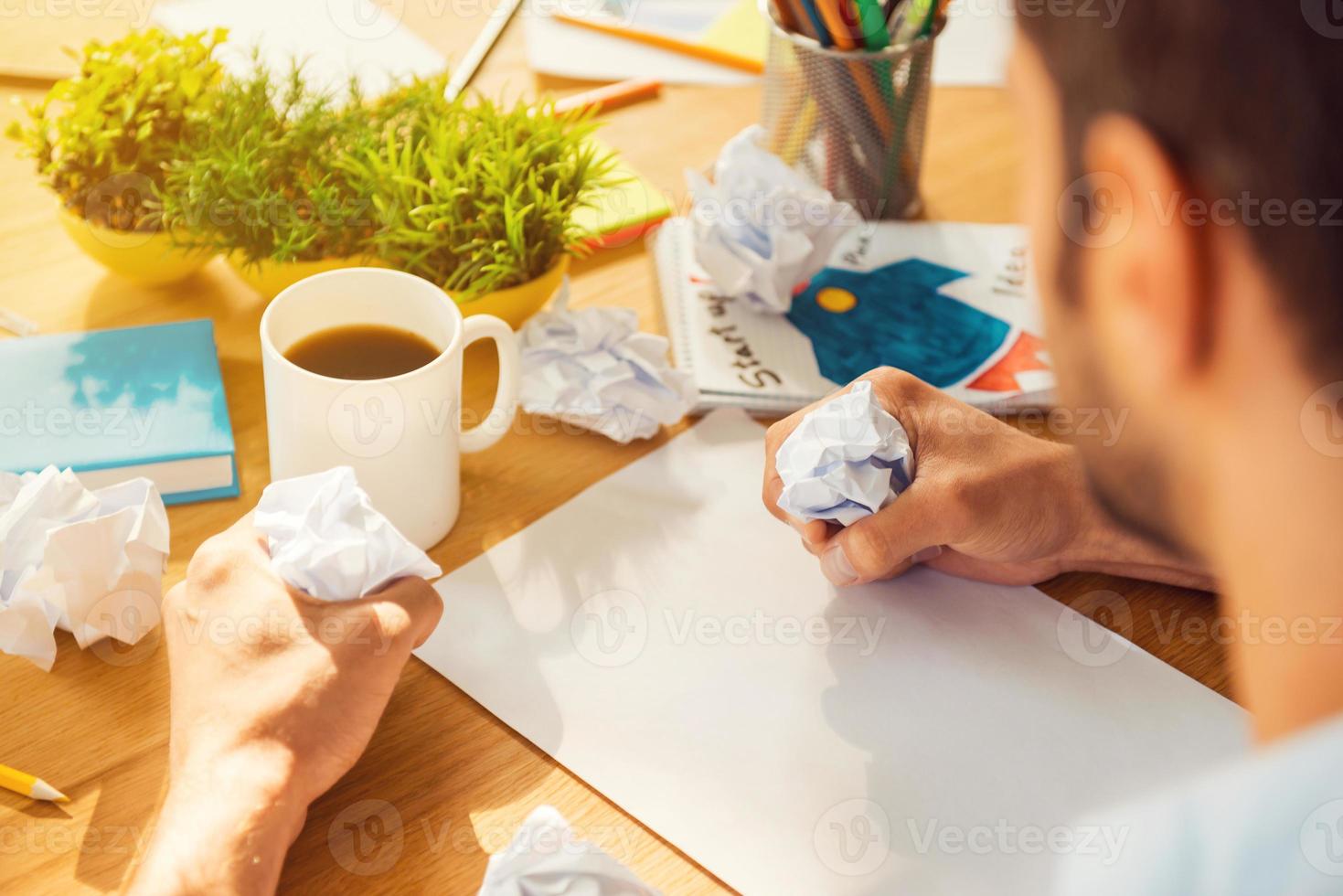 It is always hard to start. Close-up rear view of man smashing pieces of paper while sitting at his working place photo