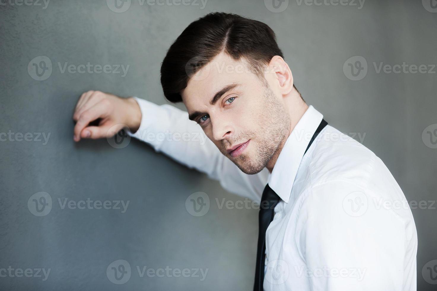 Young and confident. Handsome young man looking at camera while standing against grey background photo