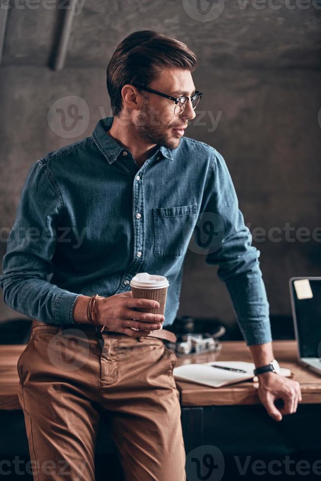Good looking young man in smart casual holding cup and looking away photo
