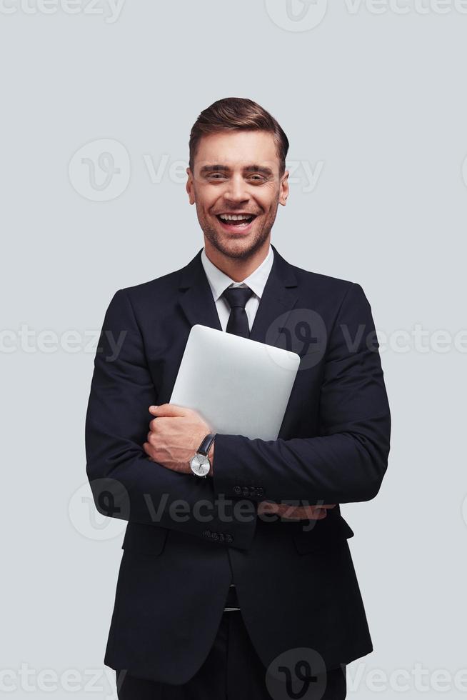 Young business professional. Handsome young man carrying digital tablet and smiling while standing against grey background photo