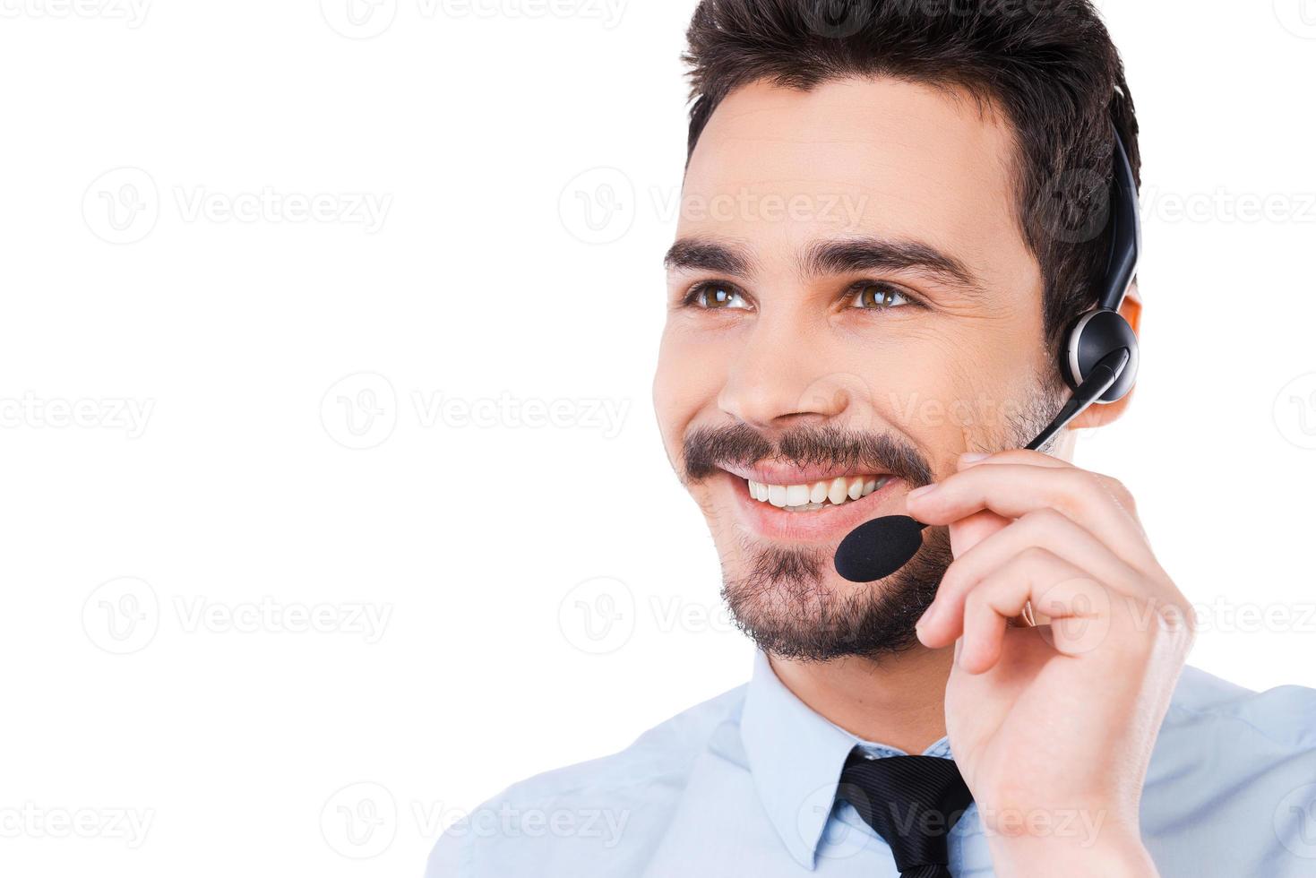 Always ready to help you. Portrait of handsome young male operator adjusting his headset and smiling while standing against white background photo