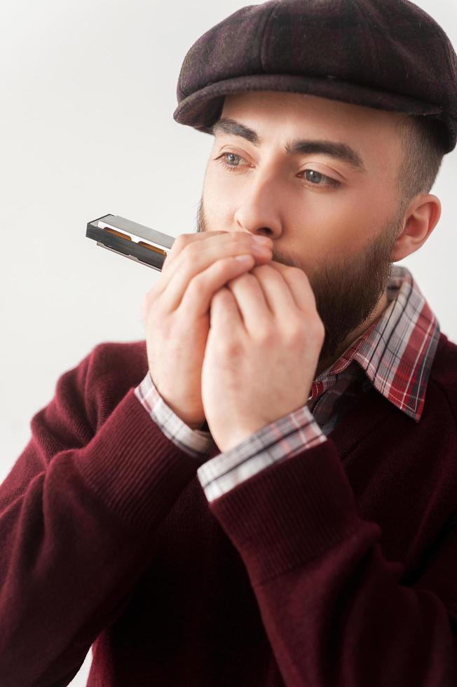 Creative soul.  Handsome young bearded men in hat playing harmonica photo