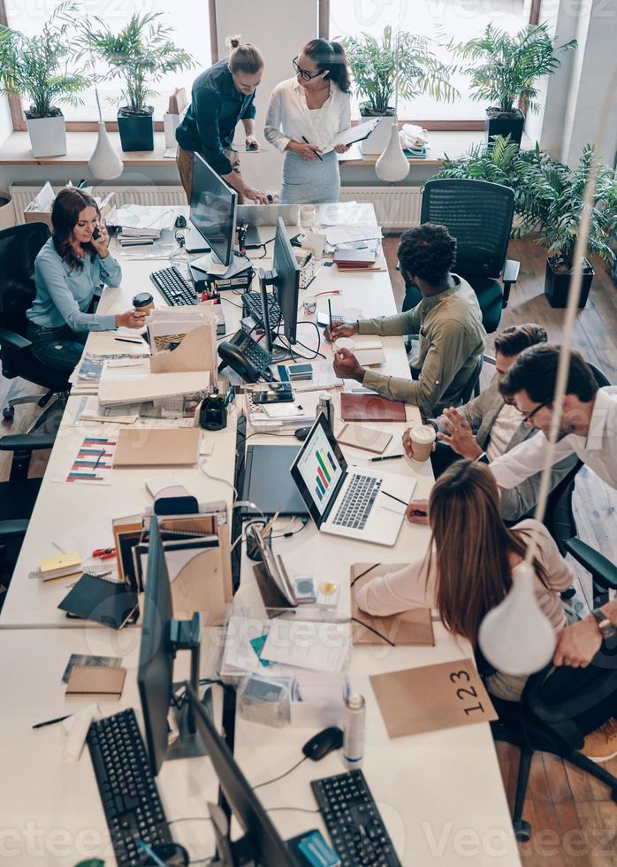 Top view of young modern people in smart casual wear communicating and using modern technologies while working in the office photo