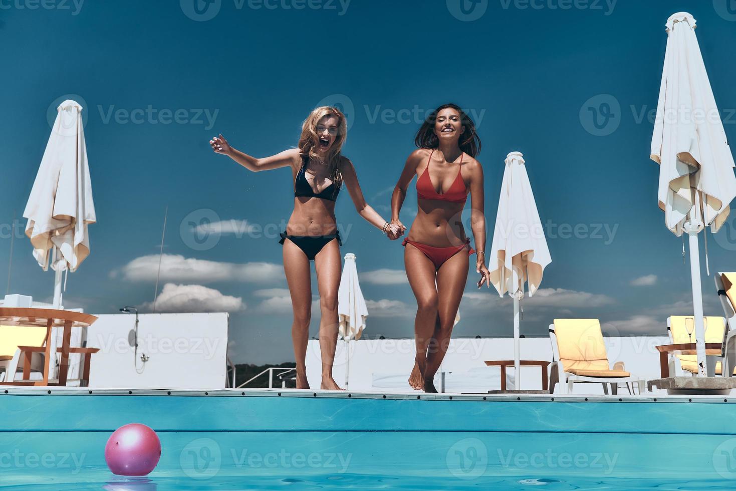 Full length of two attractive young women in bikini preparing to jump into the pool photo