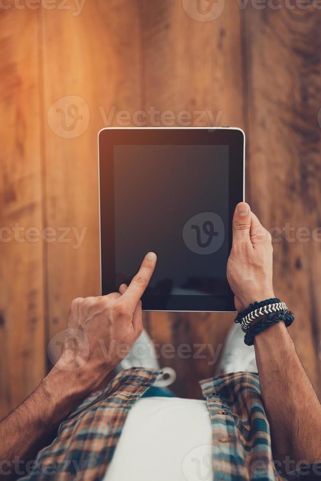 Technologies make life easier. Top view of man using digital tablet while standing on the wooden floor photo