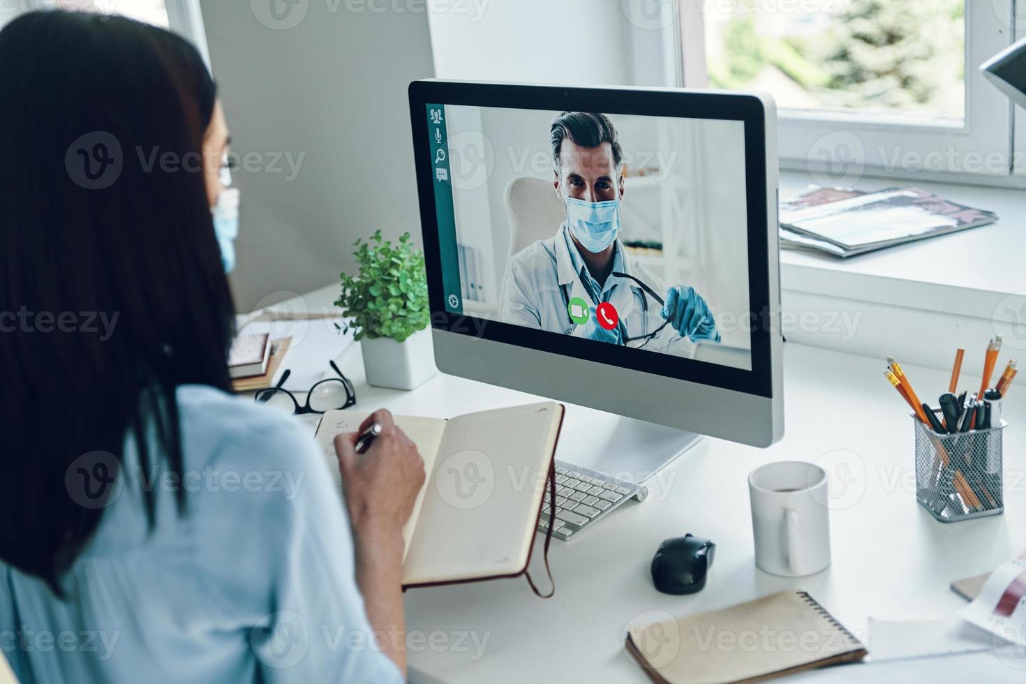 Young woman in protective face mask talking to doctor by video call photo