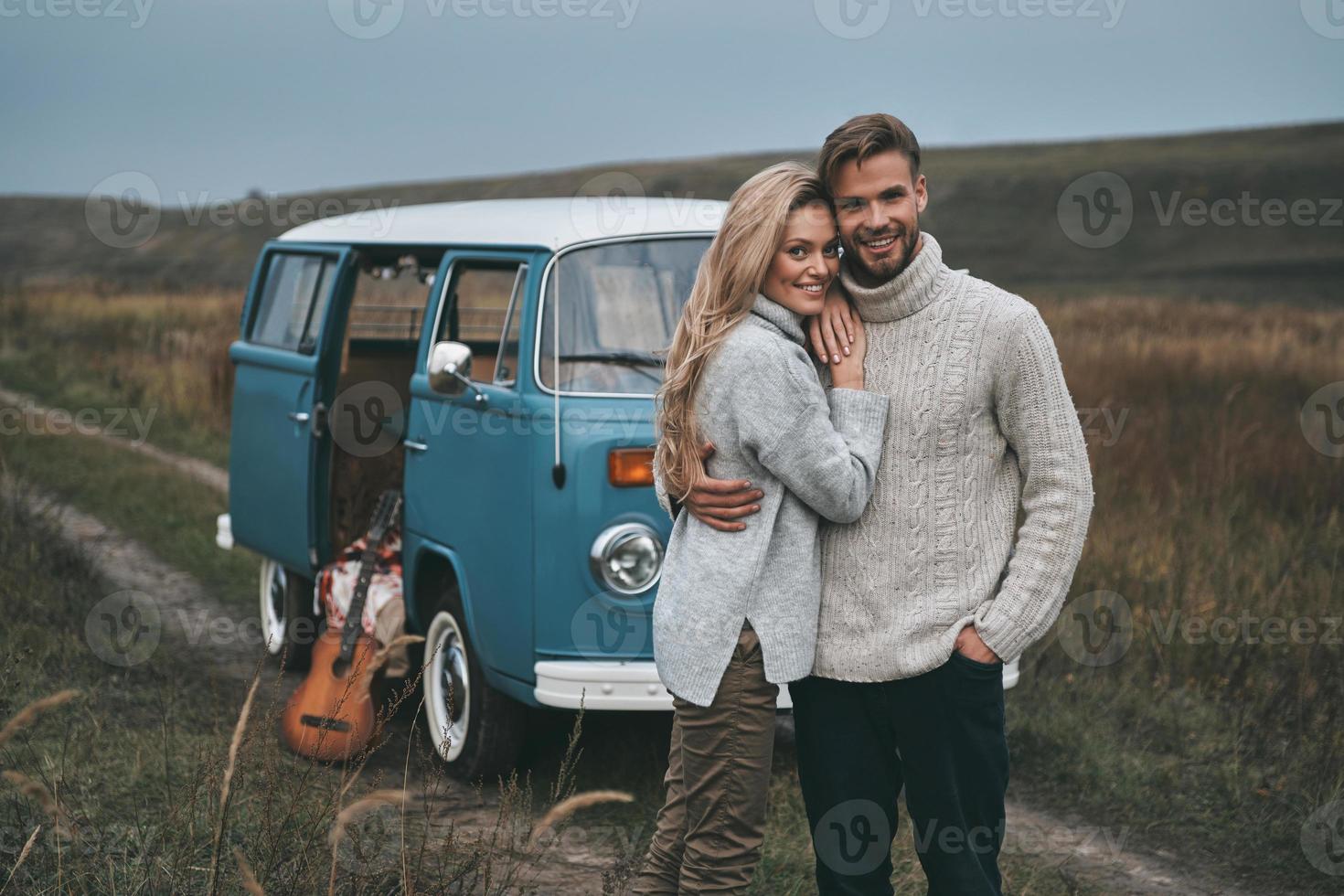 Happy to be together.  Beautiful young couple embracing and smiling while standing near the blue retro style mini van photo