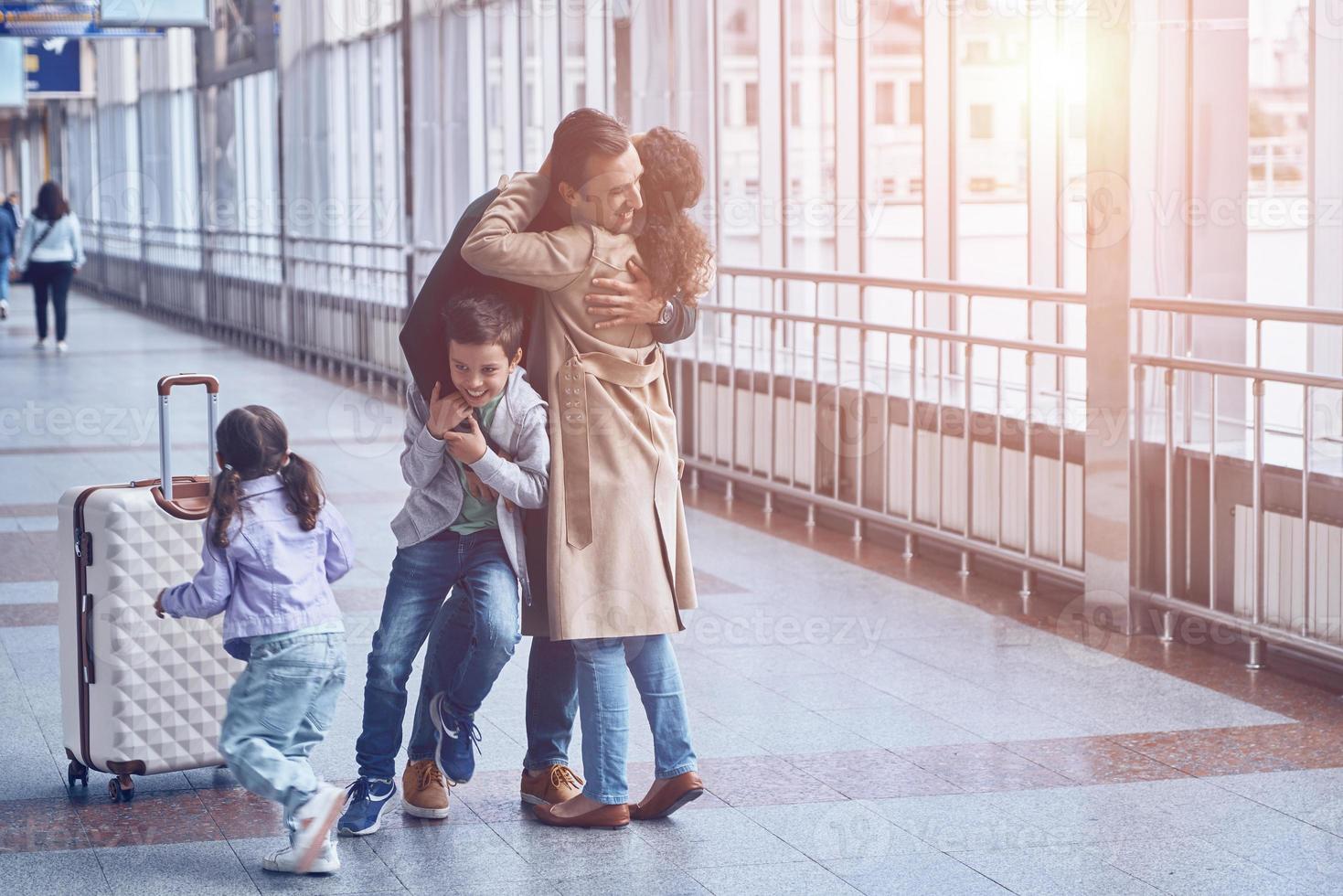 Full length of happy woman and two little kids meeting father at the airport photo