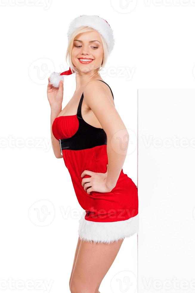 Leaning at copy space. Side view of beautiful young woman in Santa costume leaning at copy space and smiling while standing isolated on white photo