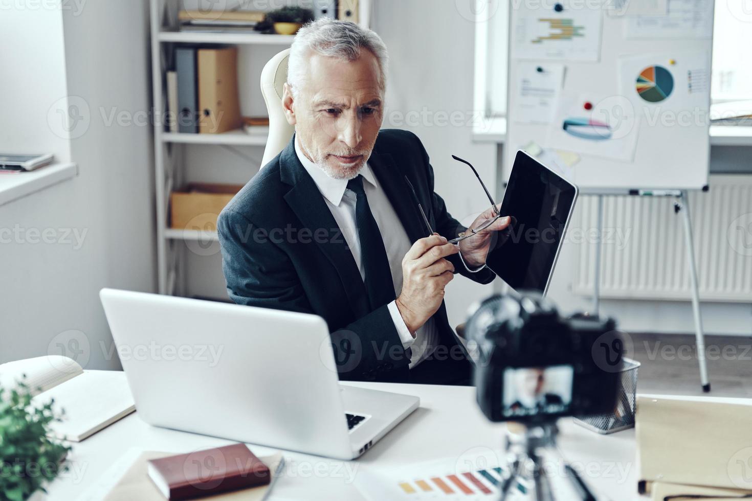Senior man in elegant business suit using digital tablet while making social media video photo