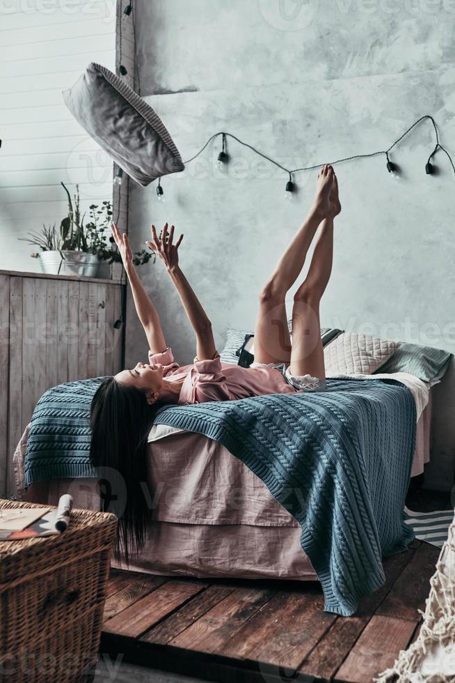 Having fun Attractive young woman throwing up a pillow and smiling while lying on the bed at