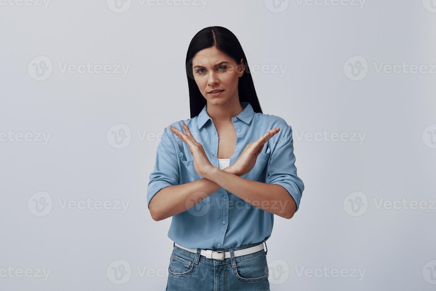Displeased young woman looking at camera and gesturing while standing against grey background photo