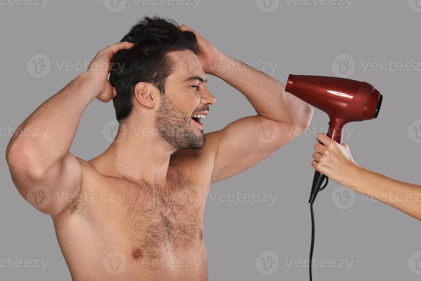 Happy man. Handsome young man drying his hair and smiling while standing against grey background photo