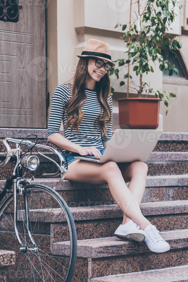 Surfing web anywhere she wants.  Beautiful young smiling woman working on laptop while sitting at the staircase near her bicycle photo
