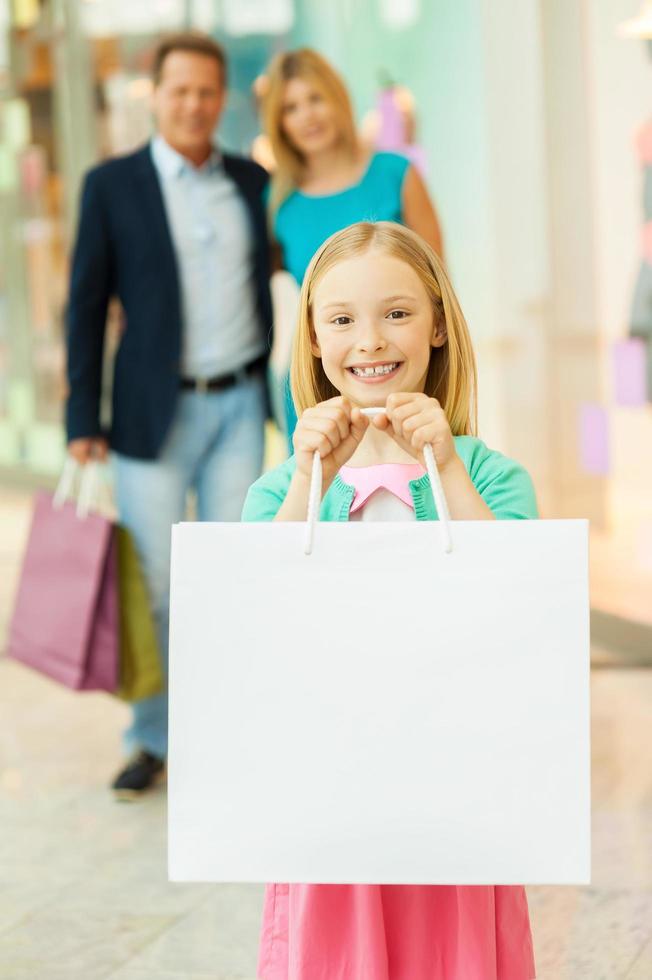 felices compras familiares. compras familiares alegres en el centro comercial mientras la niña muestra sus bolsas de compras y sonríe foto