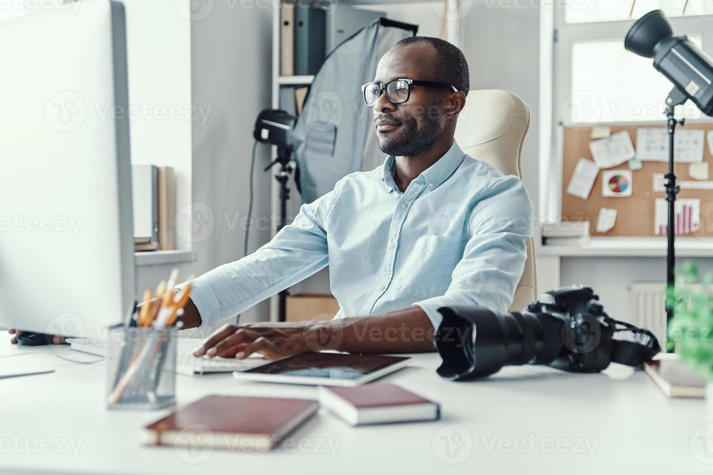 Handsome young African man using computer while working in the modern office photo